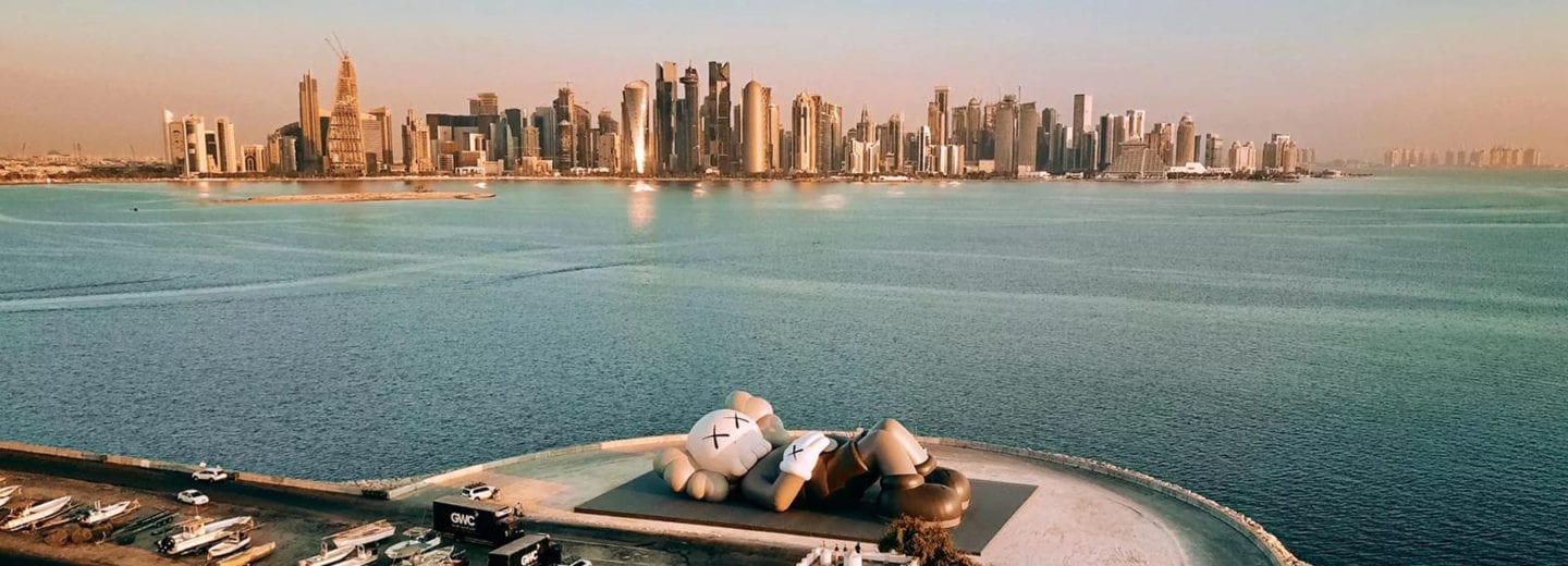 KAWS - Brian Donnelly i instalacja artystyczna na tle panoramy miasta Doha