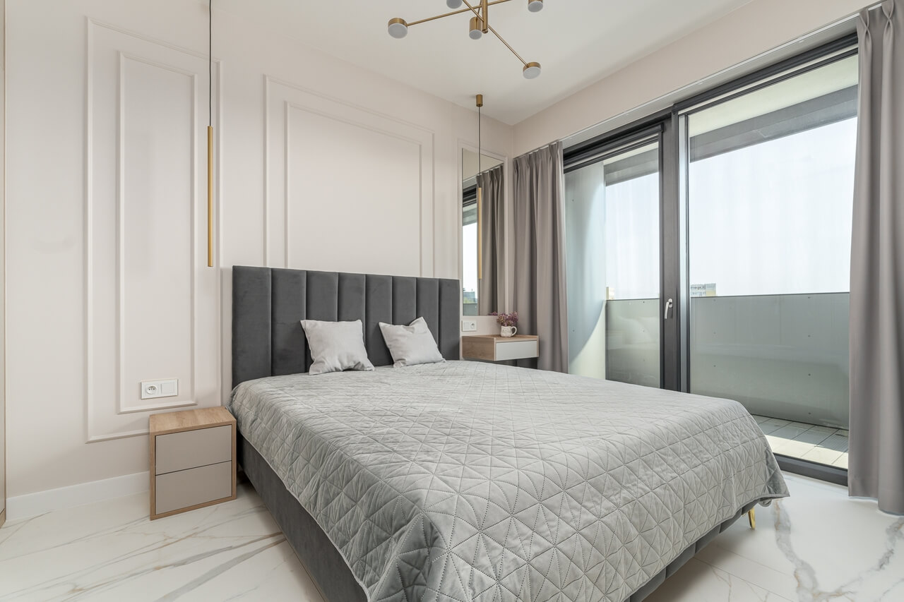 Jasna sypialnia z tapicerowanym zagłówkiem, geometrycznym oświetleniem i wyjściem na balkon