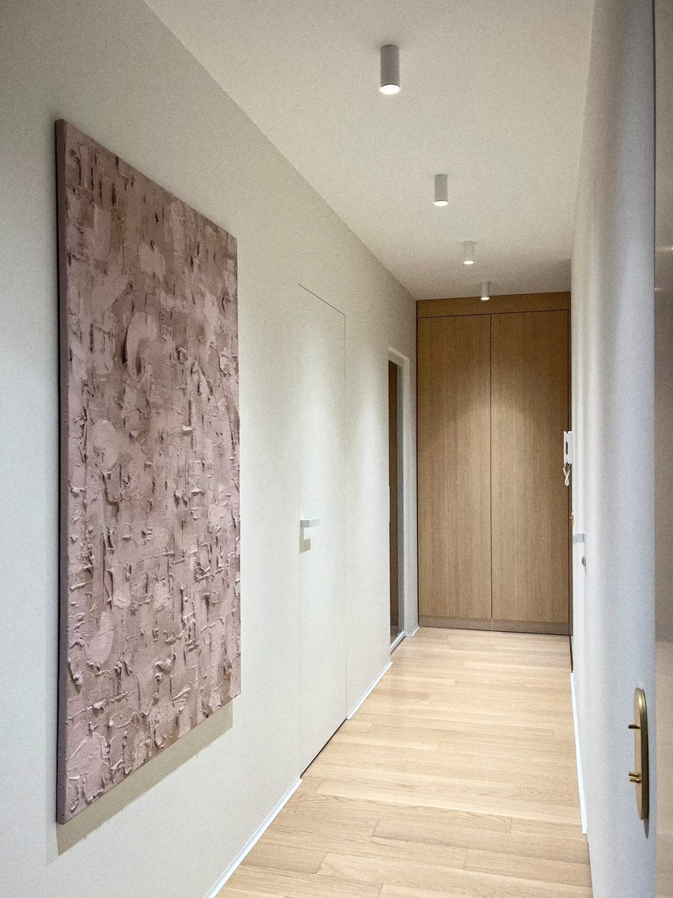 Korytarz z minimalistycznym oświetleniem i drewnianą podłogą.