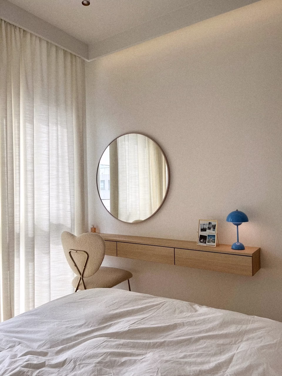 Minimalistyczna sypialnia z lustrem i designerską lampką.