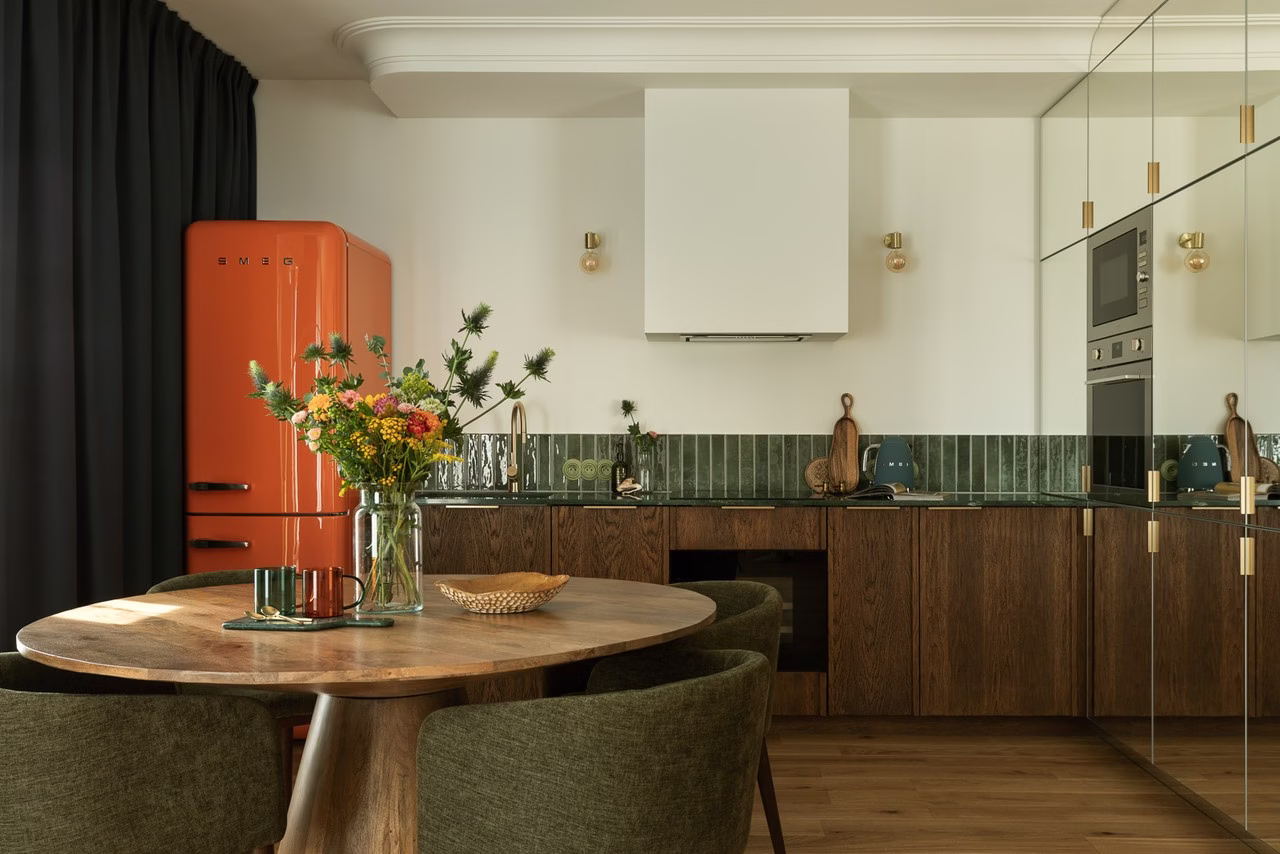 A modern kitchen with an orange refrigerator, wooden cabinets, and green tiles.
