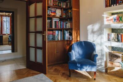 Salon z niebieskim fotelem i drewnianą biblioteką.