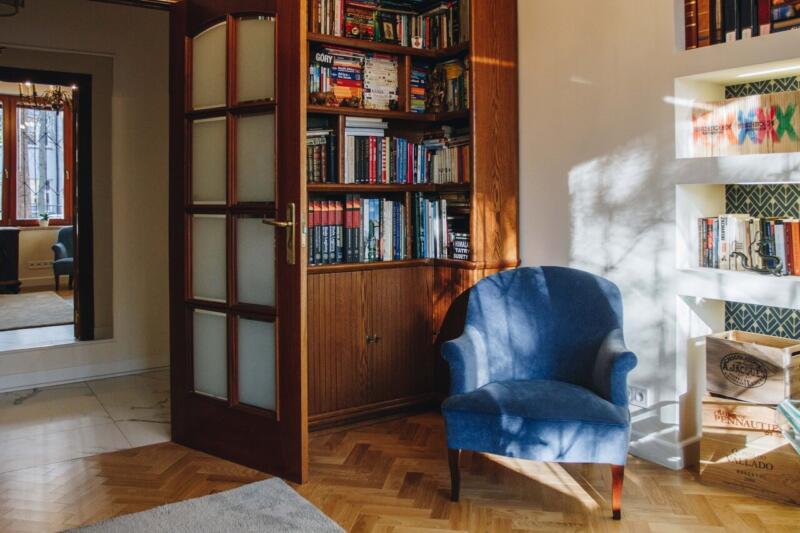 Salon z niebieskim fotelem i drewnianą biblioteką.