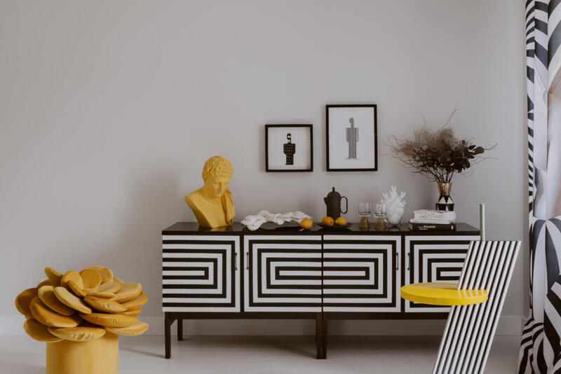 Awangardowy salon z geometryczną szafką i żółtą rzeźbą.