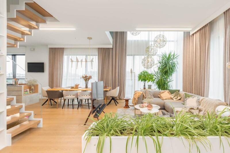Nowoczesny salon z roślinami, drewnianą podłogą i delikatnym oświetleniem.