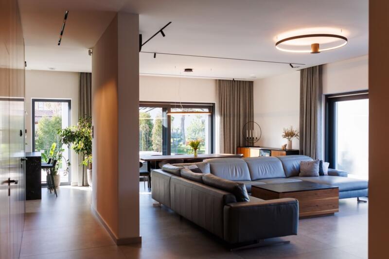 Elegancki salon z dużą sofą, nowoczesnym oświetleniem i roślinami.
