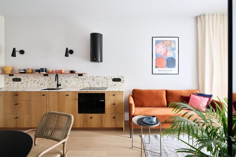 Przytulny salon z designerską kuchnią, pomarańczową sofą i plakatem.