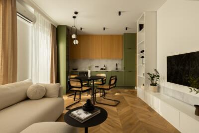 Nowoczesny salon z zieloną kuchnią i drewnianą podłogą.