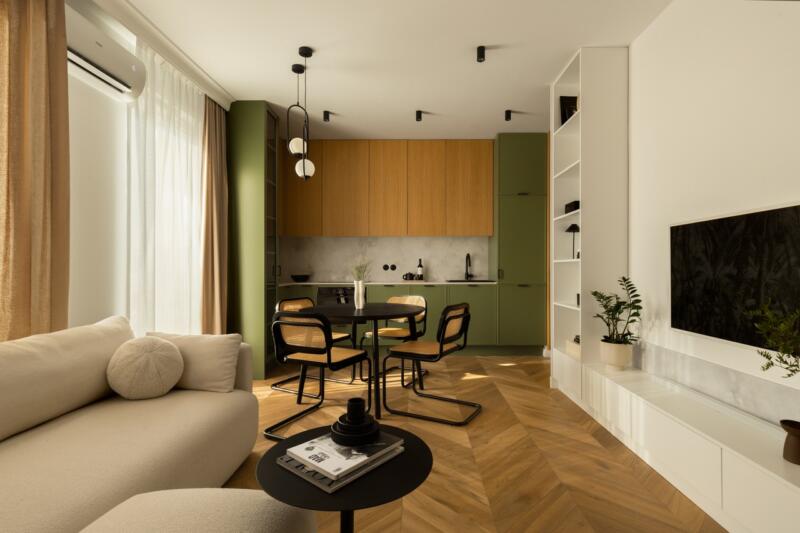 Nowoczesny salon z zieloną kuchnią i drewnianą podłogą.