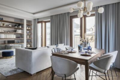 Elegancki salon z drewnianym stołem, welwetową sofą i regałami.
