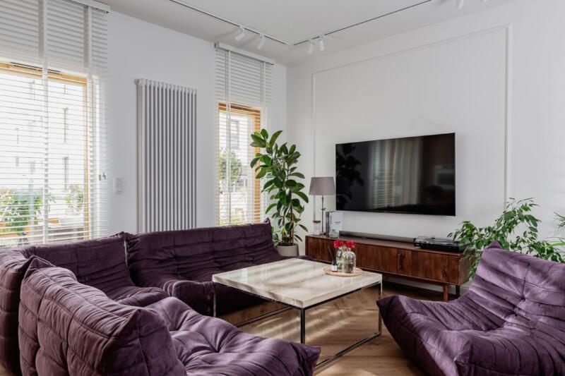 Nowoczesny salon z fioletowymi sofami, telewizorem i roślinami. Pięknie, prawda?