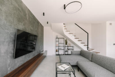 Nowoczesny salon z szarą sofą i designerskimi schodami.