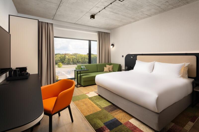 Nowoczesny pokój hotelowy z dużym łóżkiem i kolorowym fotelem.
