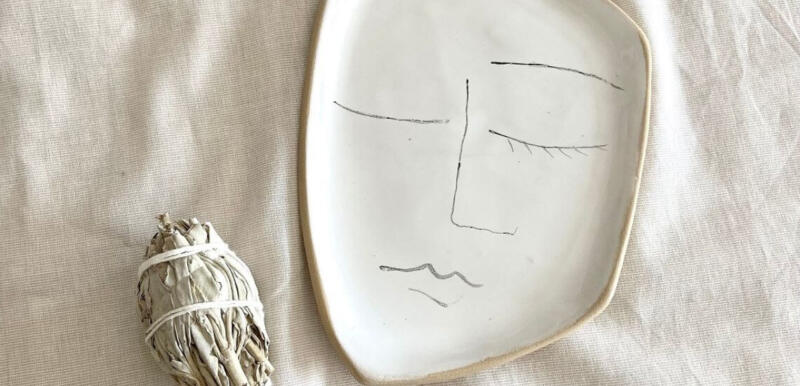 Ceramiczny talerz z rysunkiem twarzy obok białej szałwii.