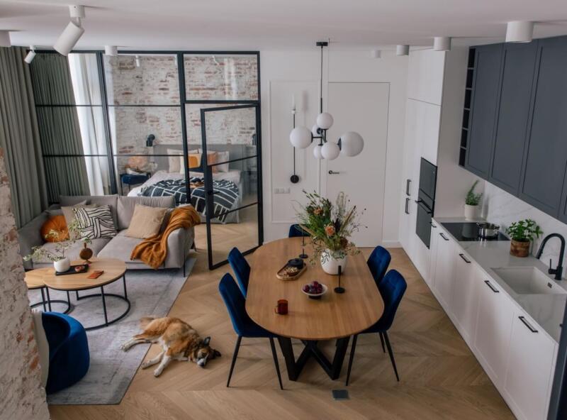 Przytulny salon z aneksem, elegancki stół i uroczy piesek na podłodze.