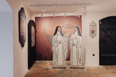 Wnętrze muzeum z grafiką zakonników i ceglaną podłogą.