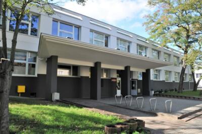 Nowoczesny budynek szkolny z zielonym otoczeniem i jasną fasadą.