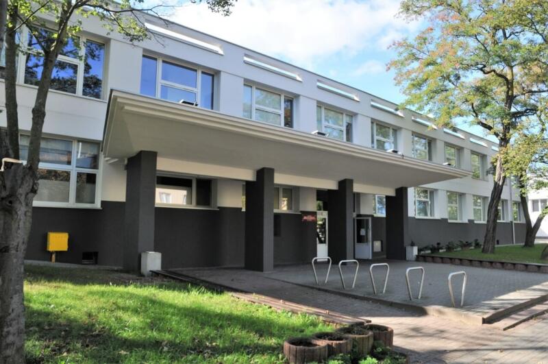 Nowoczesny budynek szkolny z zielonym otoczeniem i jasną fasadą.