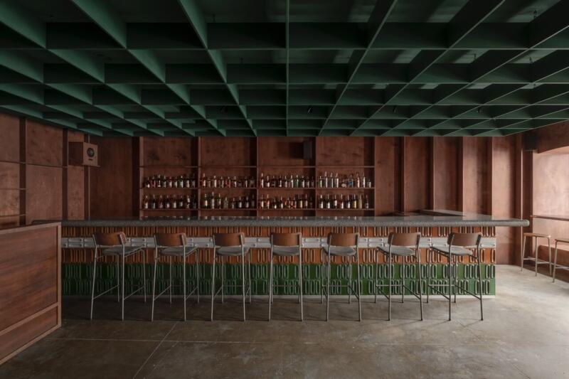 Bar w stylu industrialnym z zielonym sufitem i eleganckimi krzesłami.
