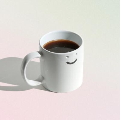 Biały kubek z uśmiechem i kawą, minimalistyczny design.