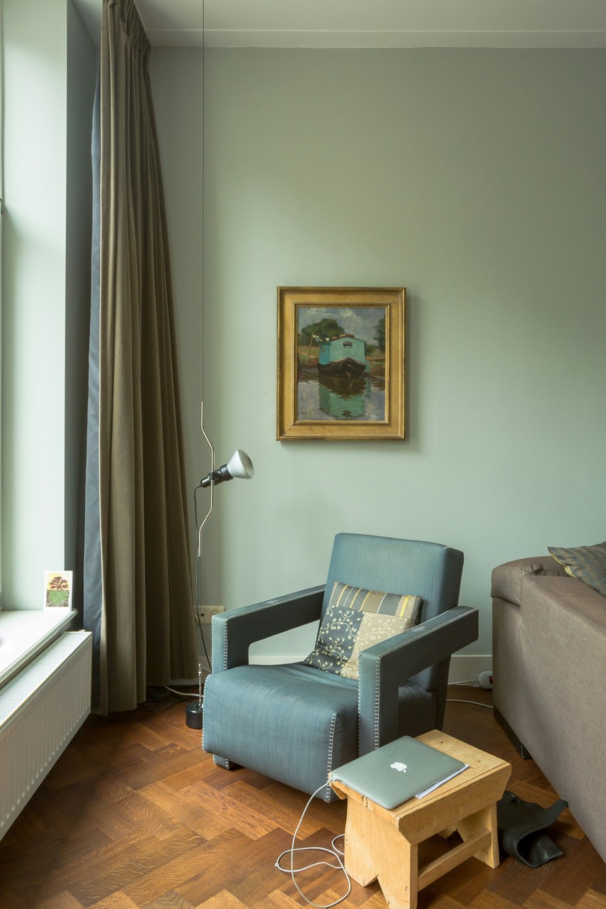 Salon z niebieskim fotelem, obrazem i drewnianą podłogą.