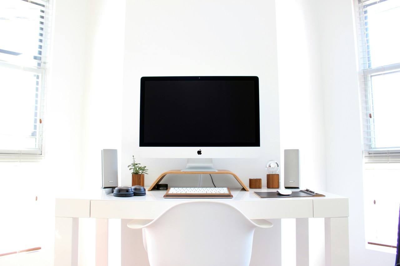 Minimalistyczne białe biurko z nowoczesnym monitorem i akcesoriami.
