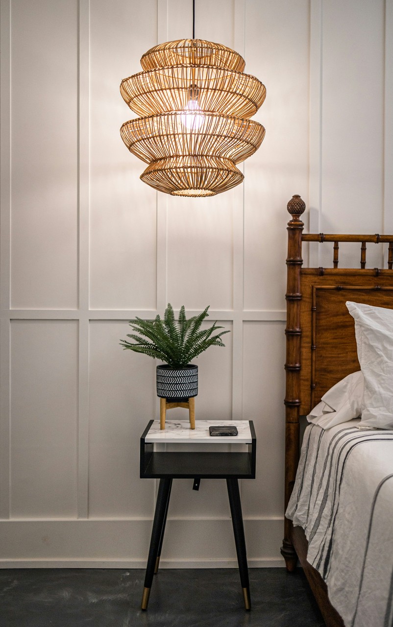Lampa boho, stylowy stolik i roślina w eleganckiej sypialni.