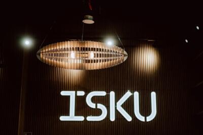 Lampa designerska nad logo ISKU, nowoczesne wnętrze z drewnem.