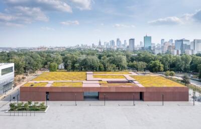 Nowoczesna architektura biurowca z zielonym dachem w tle miejskiej panoramy.