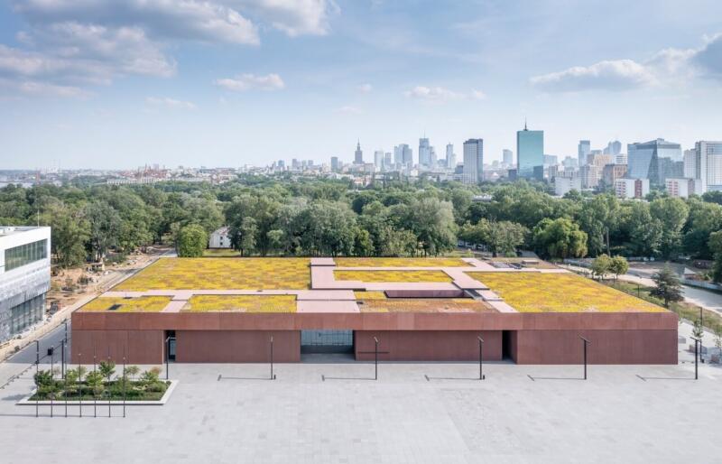 Nowoczesna architektura biurowca z zielonym dachem w tle miejskiej panoramy.
