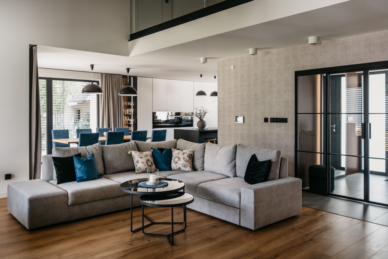 Nowoczesny salon z szarą kanapą i eleganckim stołem w tle.
