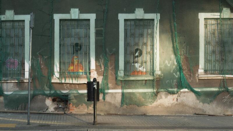 Stara fasada z graffiti i zniszczonymi oknami, osłonięta zieloną siatką.