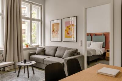 Elegancki salon z szarą sofą i designerskimi plakatami na ścianie.
