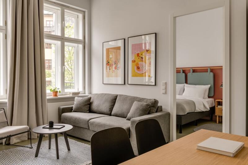 Elegancki salon z szarą sofą i designerskimi plakatami na ścianie.