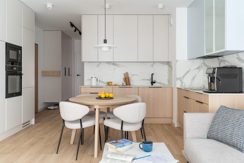 Modern kitchen with wood and marble, dining table, bright chairs.