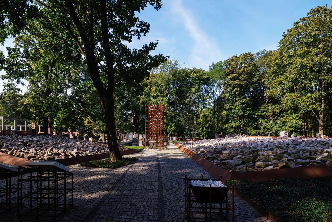 Zielony park z nowoczesną instalacją rzeźb wśród drzew i kamieni.