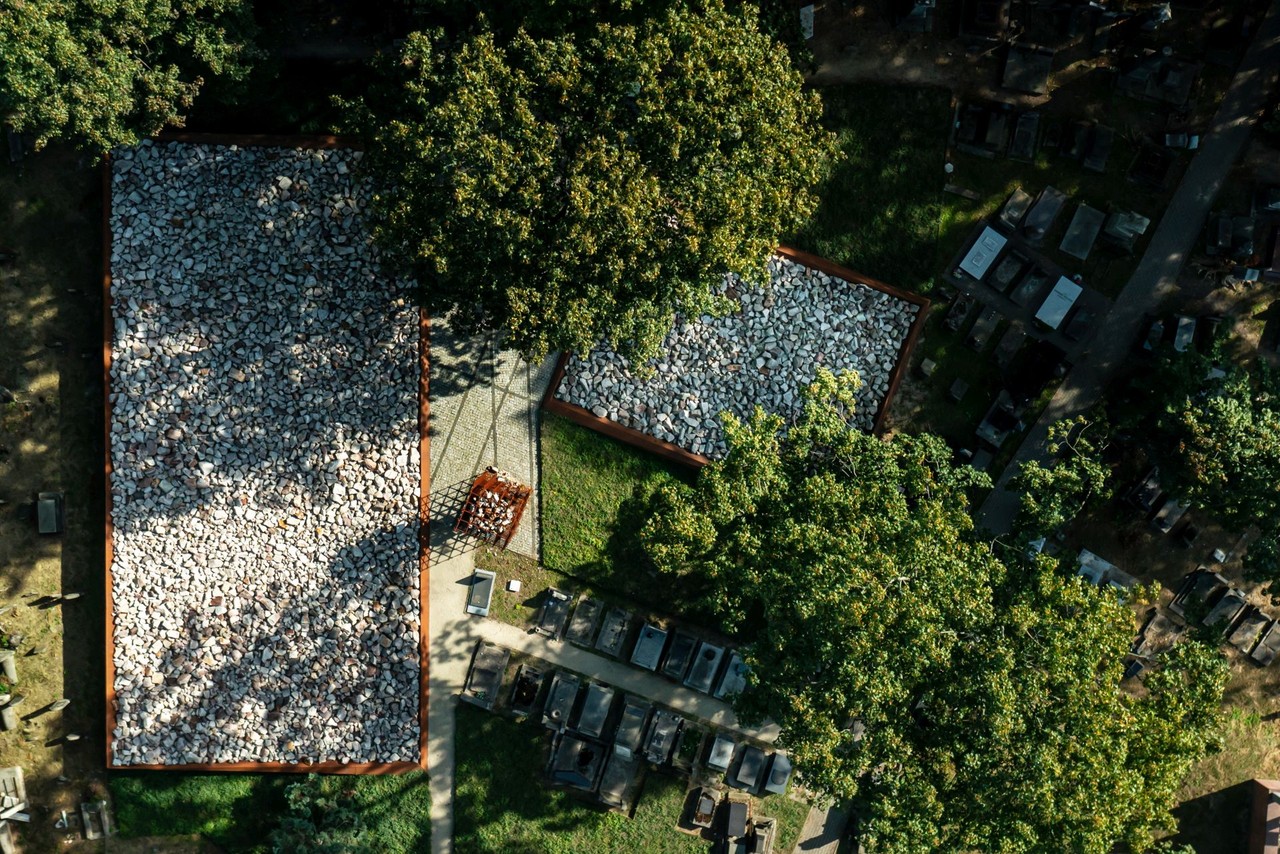 Widok z lotu ptaka na zielony plac z kamiennymi rabatami i cienistymi drzewami.