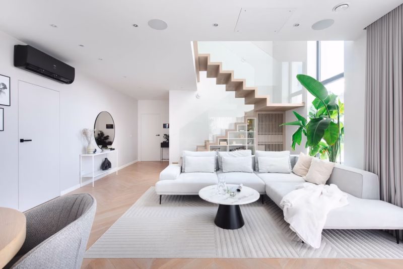 Nowoczesny salon z jasnymi meblami i szklaną balustradą schodów.