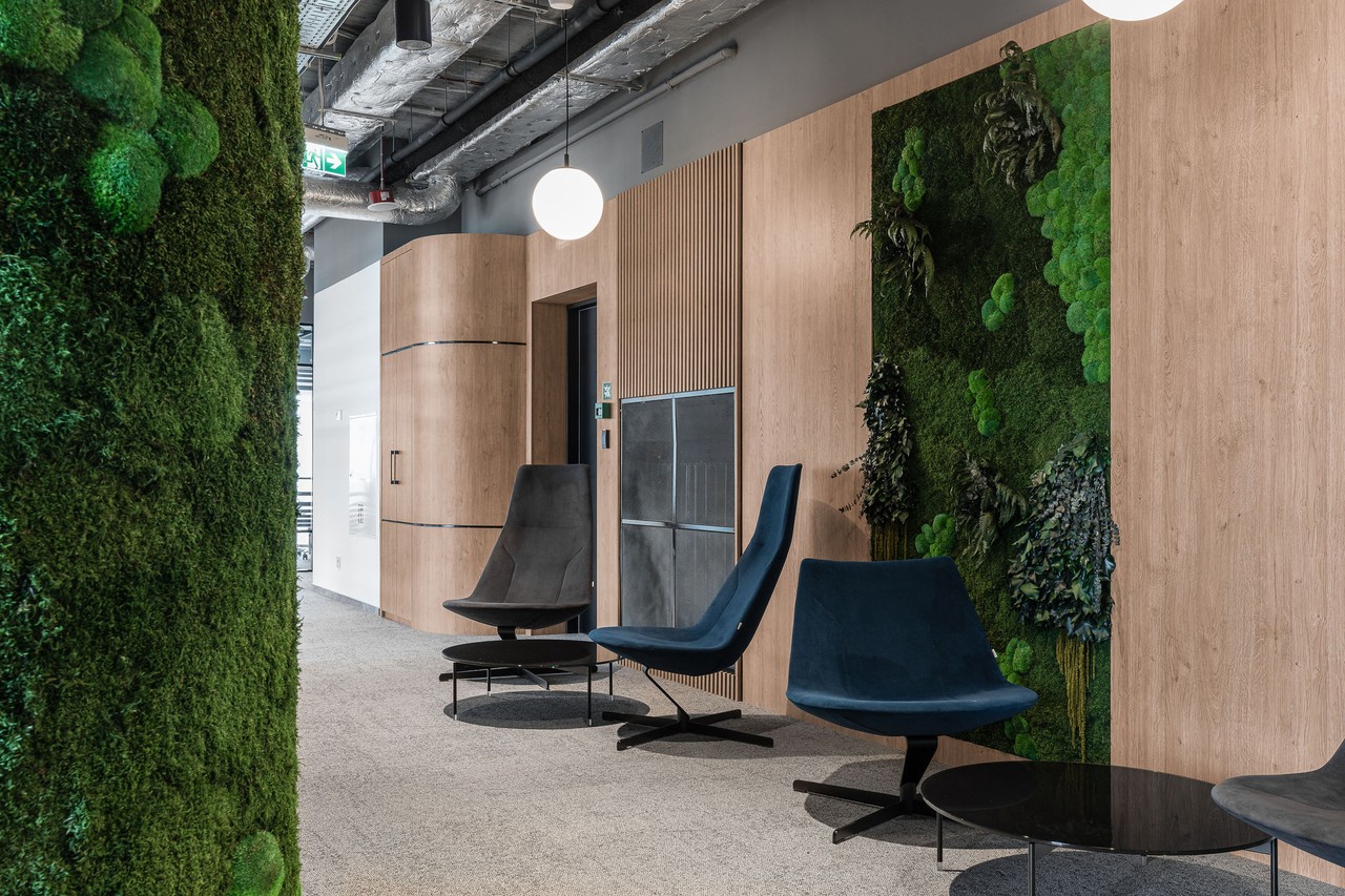 Nowoczesna przestrzeń biurowa z zieloną ścianą i designerskimi fotelami.