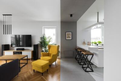 Nowoczesny salon z żółtym fotelem i designerską kuchnią.