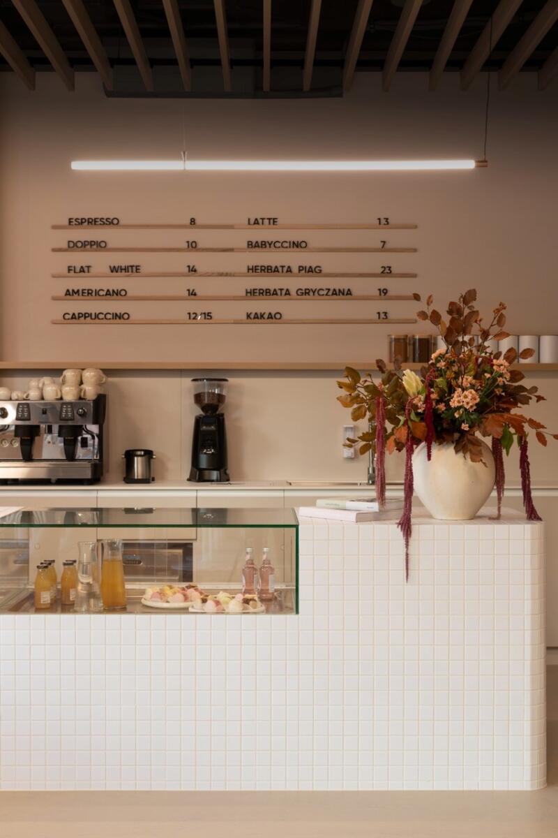 Minimalistyczna kawiarnia z menu i dekoracją kwiatową.