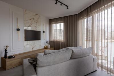 Elegancki salon z marmurową ścianą i subtelnymi beżowymi zasłonami.