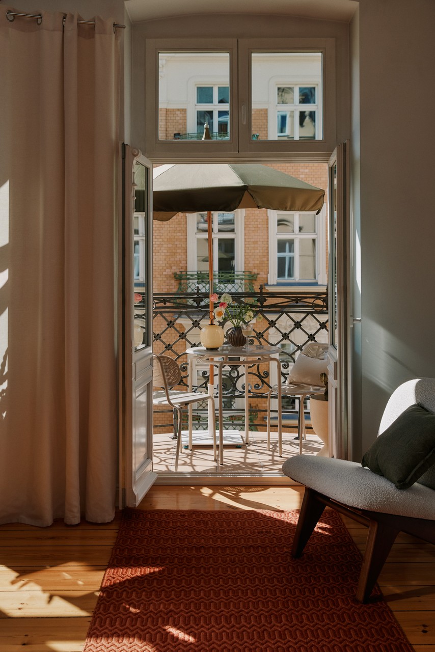 Przytulny balkon z designerskimi meblami i zielonym parasolem.