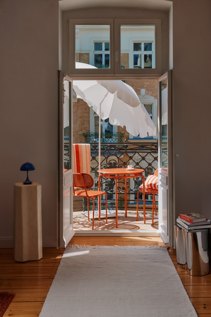 Stylowy balkon z pomarańczowymi meblami i białym parasolem.