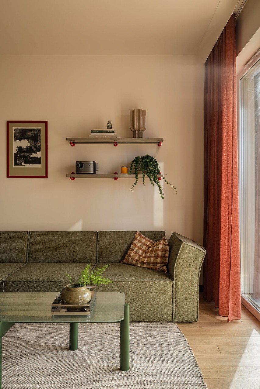 Przytulny salon z sofą, półkami i roślinami, ciepłe odcienie wnętrza.