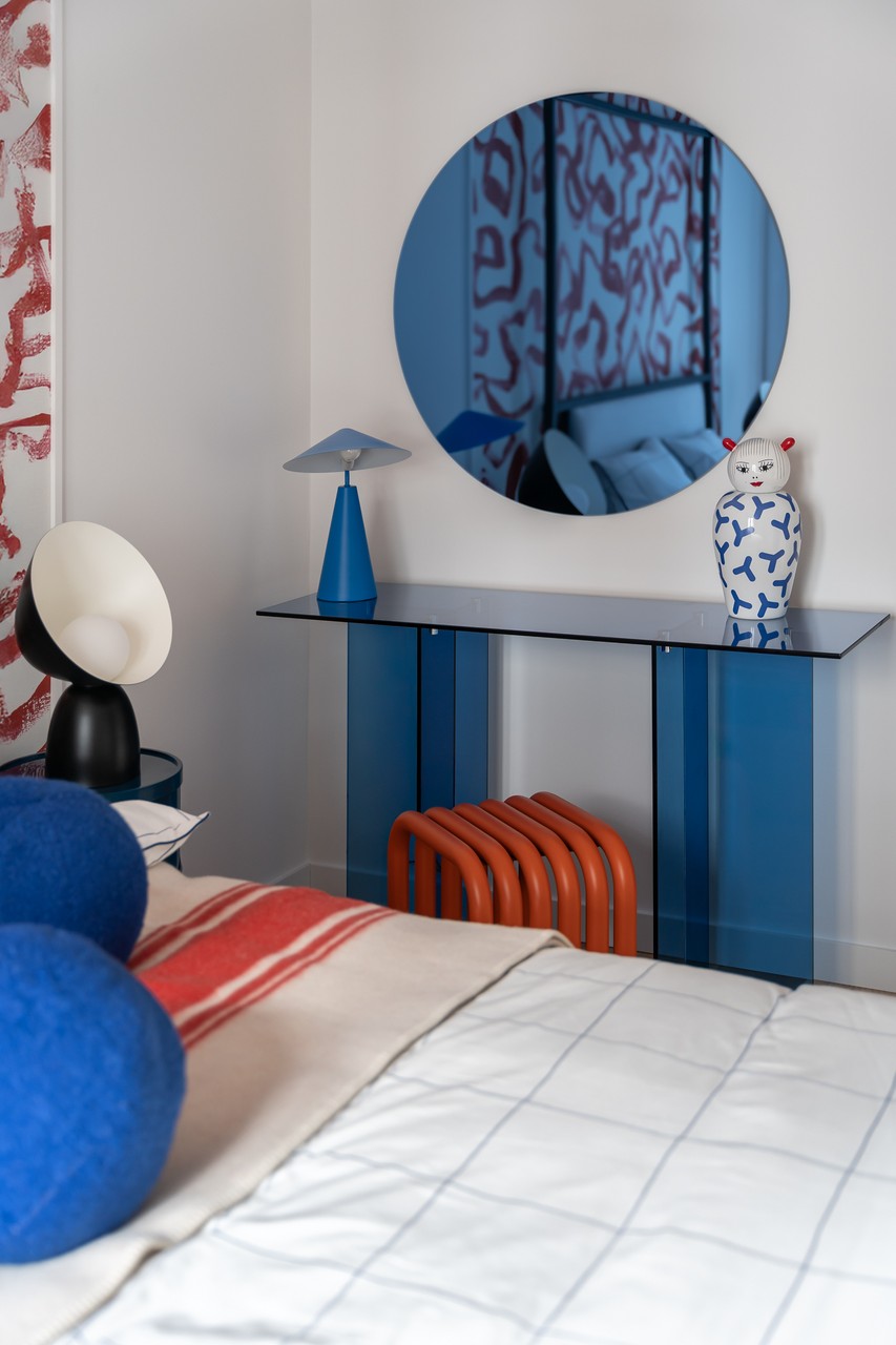 Stylowy kącik z lustrem, niebieskim stolikiem i designerską lampą.