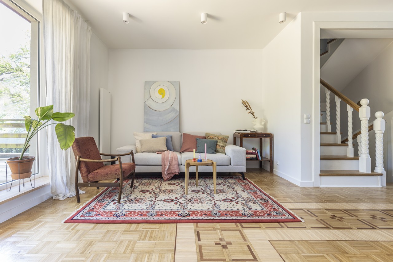 A cozy living room with a sofa, art on the wall and a colorful carpet.
