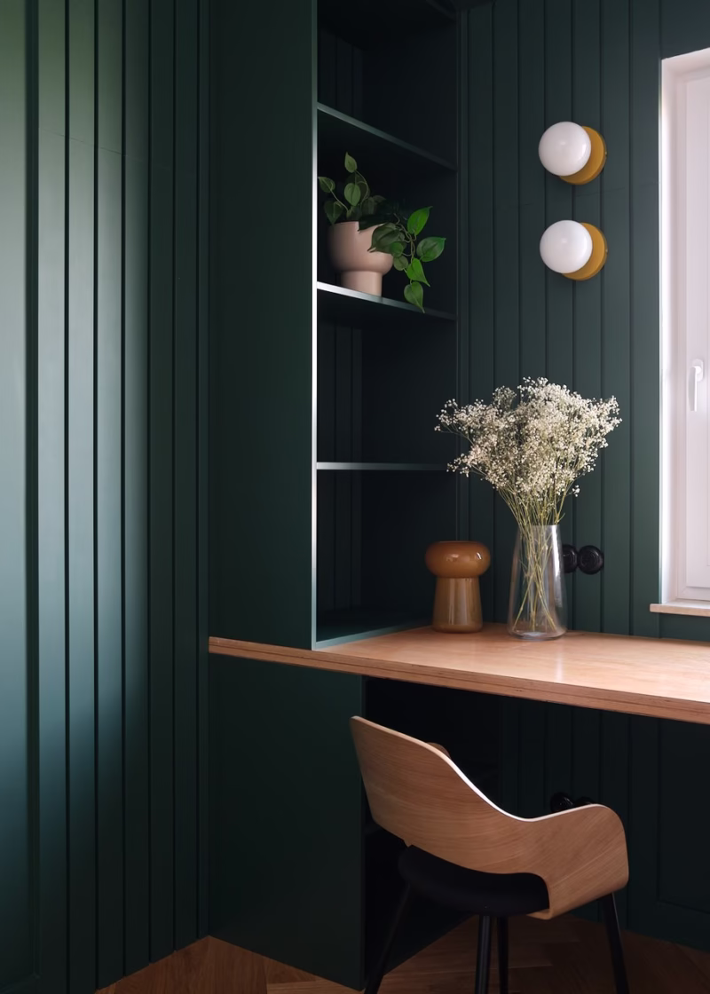 Green wall, wooden desk and elegant accessories in the study.