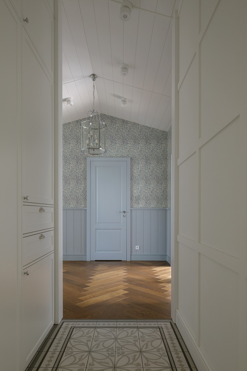 Elegancki korytarz z drewnianą podłogą i wzorzystą tapetą.