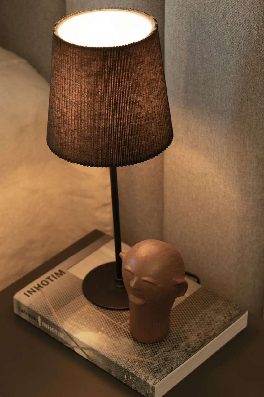 Lampa stołowa na książce, obok minimalistyczna drewniana rzeźba.